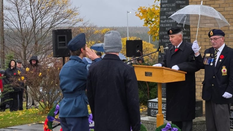 People dressed in military attire stand near wreaths with poppies