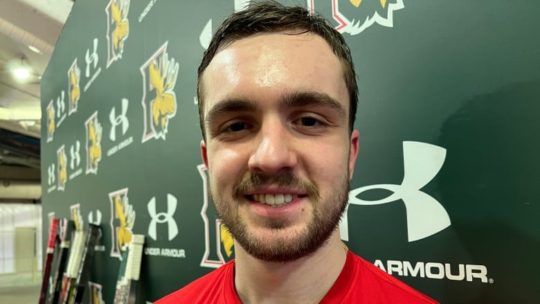 A bearded hockey player wearing a red shirt smiles after a game.