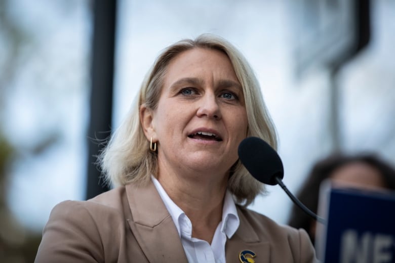 A white woman with white-blond hair speaks into a mic.