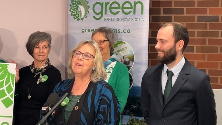 Elizabeth May stands in front of a microphone with Anthony Edmonds to her left. 