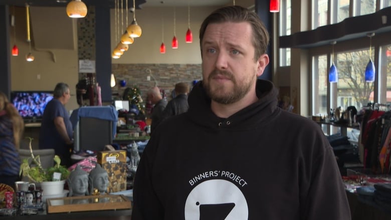 A man wearing a hoodie that reads 'Binners' Project' looks on in an indoor market.