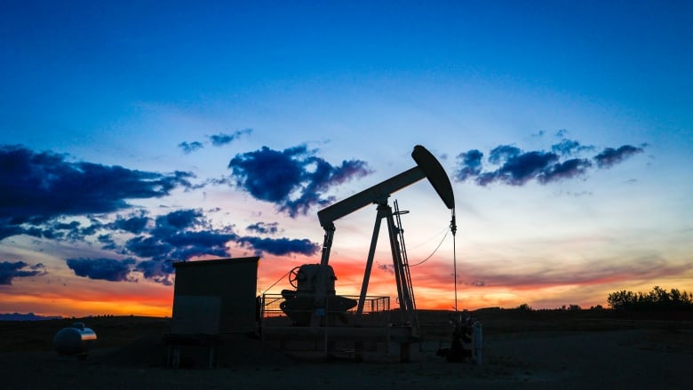 A pumpjack stands in shadow with a colourful sunset in the background.