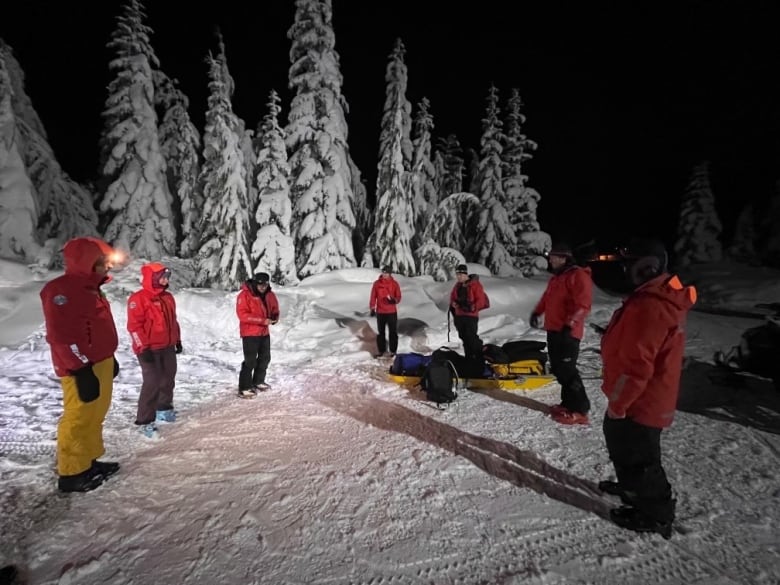 A group of people in high vis orange winter jackets stand outside in the snow.