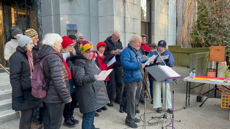 About a dozen people gather by a podium and read off pieces of paper.