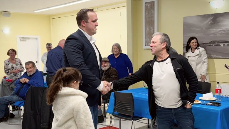 two men shake hands in a room of tables 