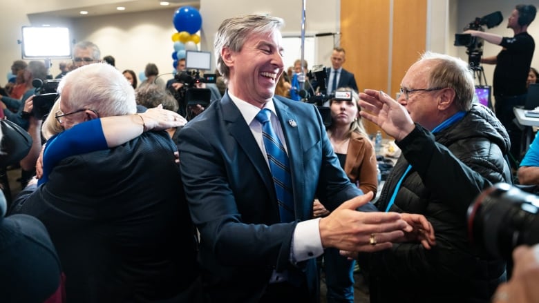 A man smiles and supporters hug around him.